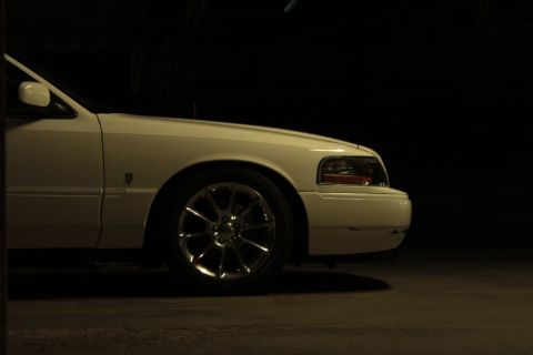 2000 Mercury Grand Marquis - A white 2000 Mercury Grand Marquis is shown from the front quarter panel, highlighting its distinctive wheel design.