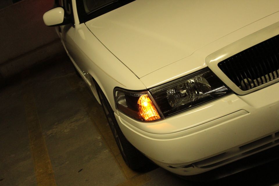 White 2000 Mercury Grand Marquis front corner, showing headlight and grille. The car is parked indoors
