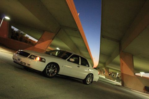 2000 Mercury Grand Marquis - A white sedan with custom wheels is parked beneath a concrete overpass as the sky darkens.