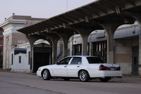 2000 Mercury Grand Marquis - A white sedan is parked on a street next to a building with a covered walkway.
