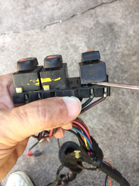 1989 Ford Bronco - A hand holds a window and door lock control switch assembly with visible wiring and three buttons.