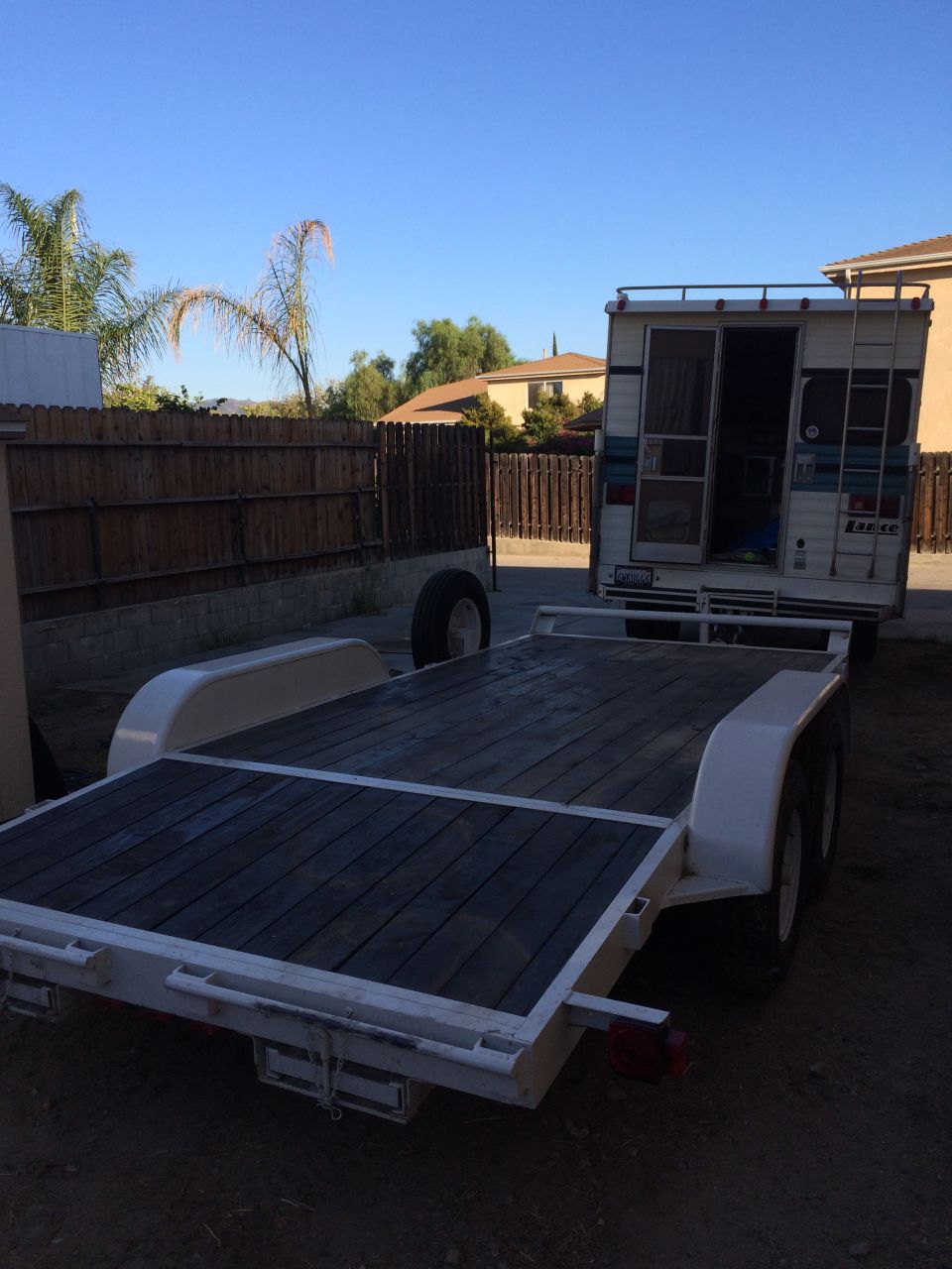 Empty tandem-axle flatbed car trailer parked in a dirt yard