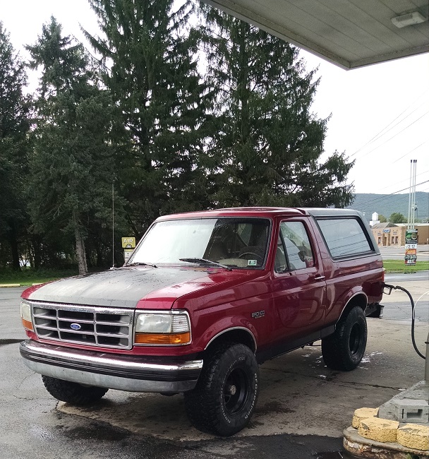 Red Ford Bronco with a grey hood at a gas station