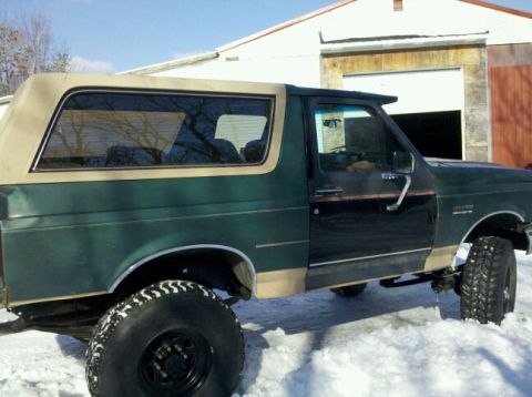 1990 Ford Bronco - This Ford Bronco is parked in the snow, showing its side profile and tan trim.