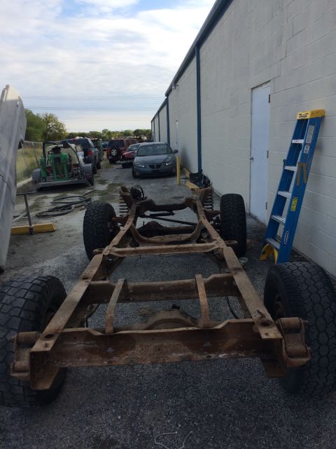 1978 Ford Bronco - The bare frame of a vehicle sits on the ground next to a building, with other cars and equipment visible.
