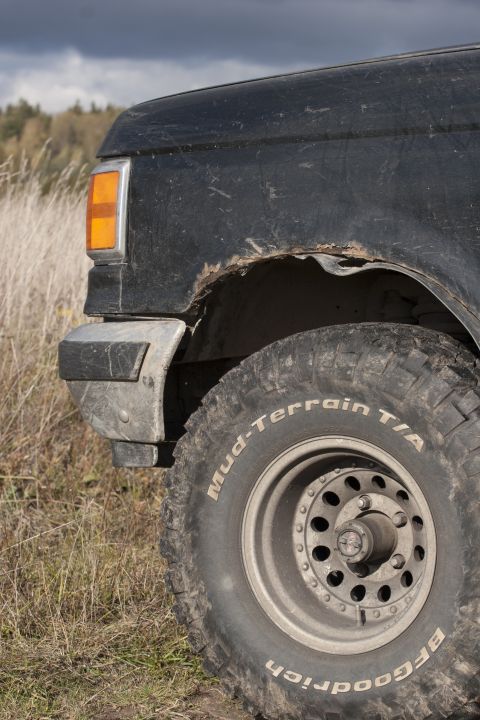 1987 Ford Bronco - A black SUV's front fender and tire are visible against a cloudy sky and dry grass.