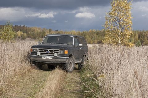 1987 Ford Bronco - A black 1987 Ford Bronco navigates a path through a dry, grassy field under a cloudy sky.
