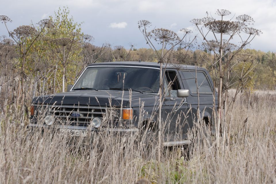1987 Ford Bronco parked in a field of dry grass and weeds