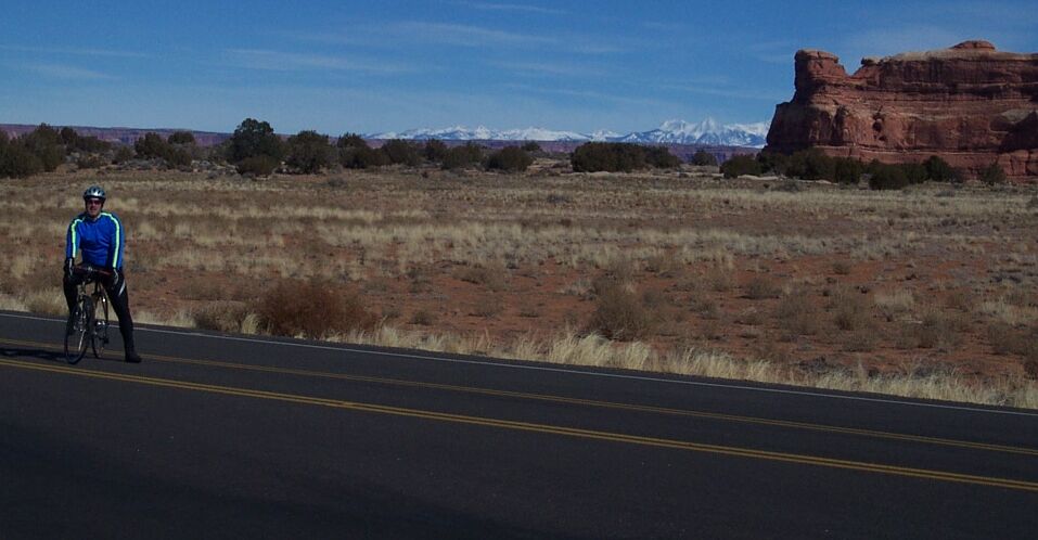 cyclist on road with desert landscape and red rock formations in background