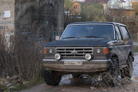 1987 Ford Bronco - A 1987 Ford Bronco is shown from the front, equipped with large off-road tires and parked on a dirt road.