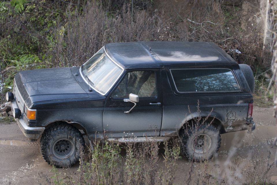 Black 1987 Ford Bronco driving through mud and brush