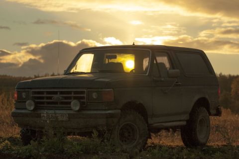 1987 Ford Bronco - An SUV sits in a field as the sun sets, casting a warm glow.