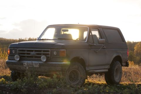 1987 Ford Bronco - A 1987 Ford Bronco is seen from a three-quarter front view, parked in a dry, outdoor landscape during sunset.