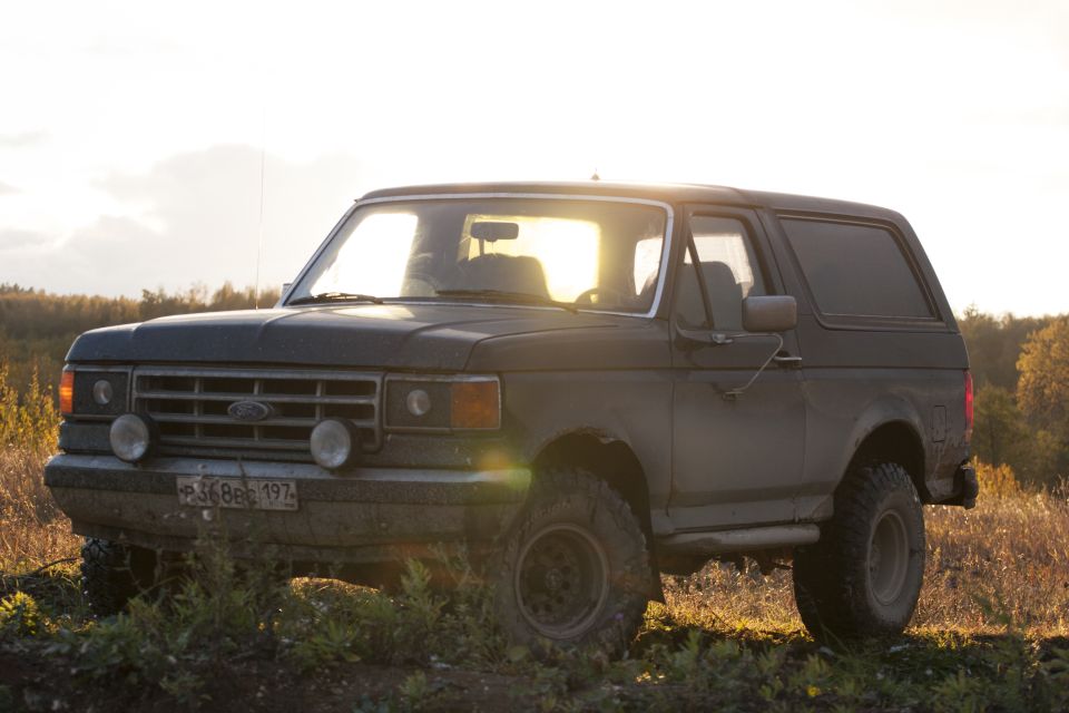 Dark 1987 Ford Bronco parked on a dirt road with a sunset in the background