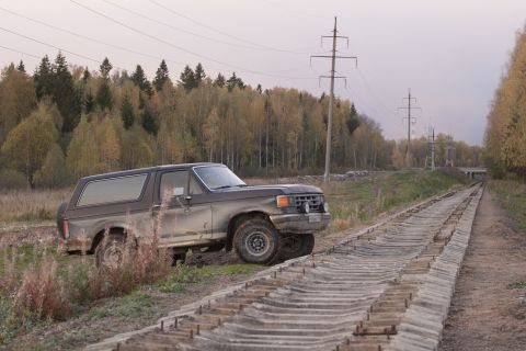 1987 Ford Bronco - A pickup truck sits parked on the side of a road with autumn foliage in the background.