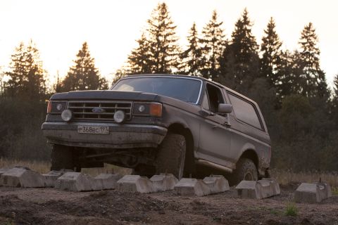 1987 Ford Bronco - An SUV navigates a rough dirt road surrounded by trees.