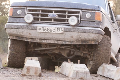 1987 Ford Bronco - 1987 Ford Bronco front end, covered in dirt, with two round fog lights.