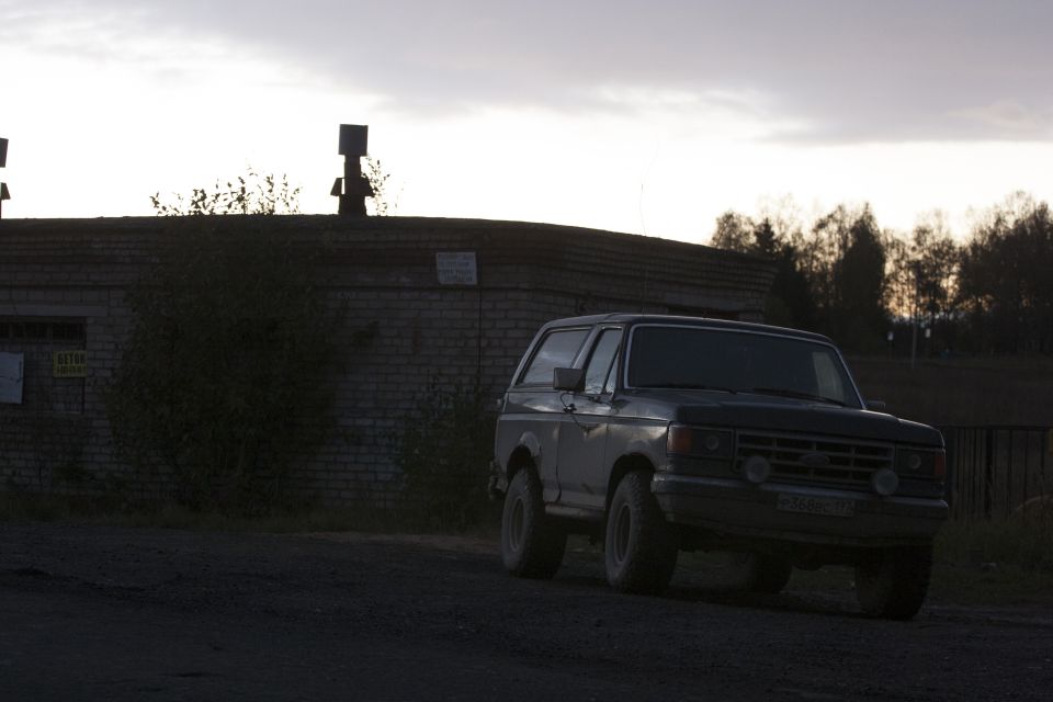 1987 Ford Bronco, dark color, front 3/4 view, slightly blurry, overcast sky