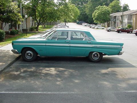 1964 Mercury Comet - A teal 1964 Mercury Comet sedan is parked in a lot with apartment buildings in the background.