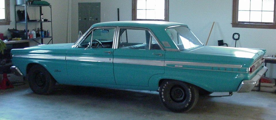 Teal 1964 Mercury Comet sedan with chrome trim and black wheels parked in a garage