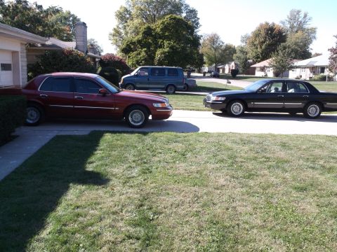 1999 Mercury Grand Marquis - Two sedans and a minivan are parked in a suburban driveway on a sunny day.