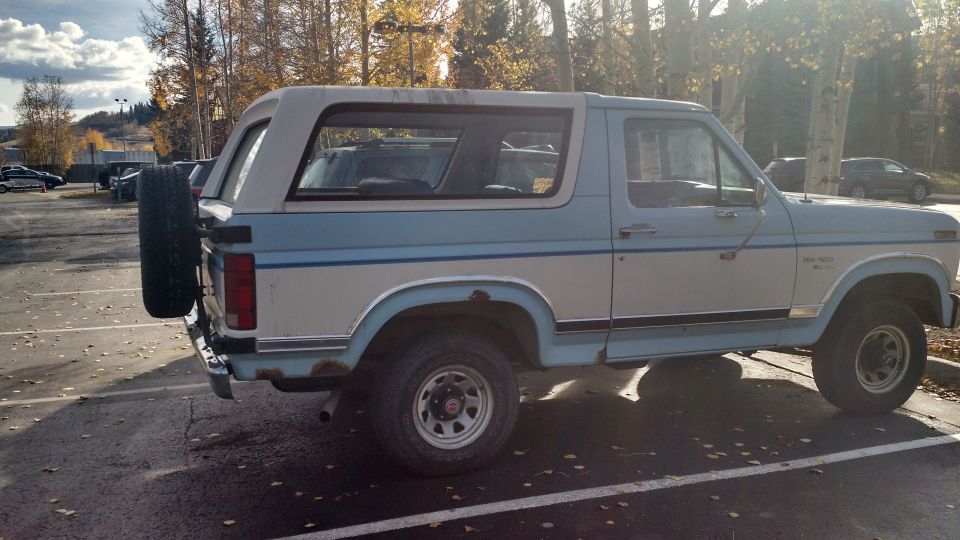 Blue and white Ford Bronco with a spare tire mounted on the rear, parked in a lot