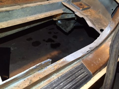 1991 Ford Bronco - The floor pan of a 1991 Ford Bronco exhibits severe rust and holes, revealing the dark ground beneath.