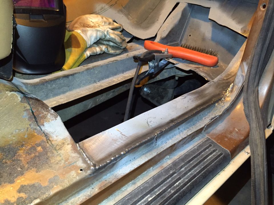 Welding equipment and gloves on a vehicle's rusty floor pan during repair