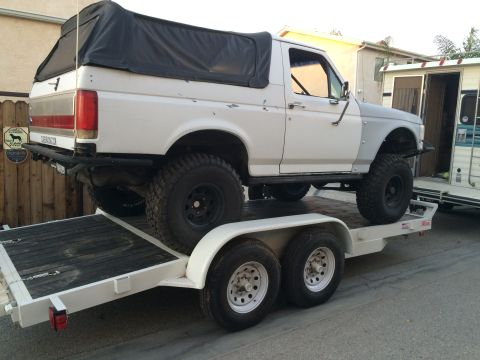 1997 Dodge 3500 - A white Ford Bronco with a black soft top is loaded onto a trailer, showing off its off-road modifications.