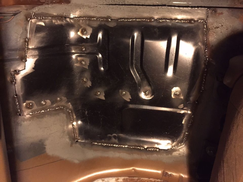 Welded metal patch on a vehicle floor pan, showing rough welds and bolt holes