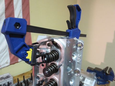 1996 Ford Bronco - A close-up of an engine cylinder head being worked on, with valve springs compressed by a clamp.