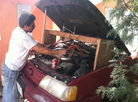 1993 Ford Taurus - A person works on the engine of a 1993 Ford Taurus SHO, which is supported by a wooden frame and chains.