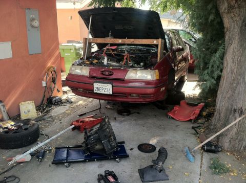 1993 Ford Taurus - A red Ford Taurus is undergoing engine repair, with the hood open and the engine removed and placed on a dolly.