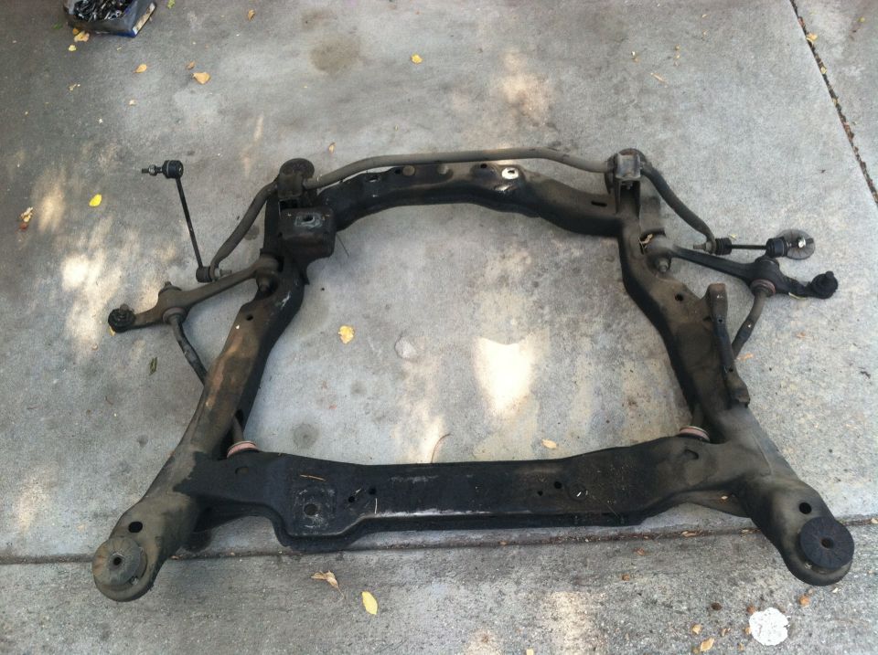 car's front subframe assembly with suspension components attached, lying on concrete