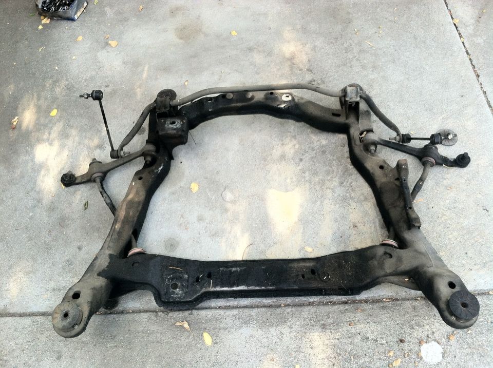 Black metal subframe assembly with tie rods and sway bar links, lying on concrete