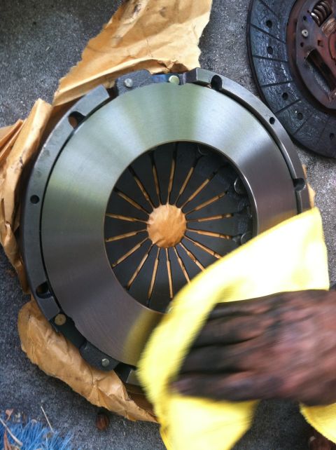 1993 Ford Taurus - A clutch disc and pressure plate are shown, with a hand cleaning the disc with a yellow cloth.