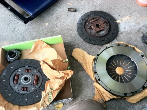 1993 Ford Taurus - Clutch disc and pressure plate parts are laid out on a concrete surface.
