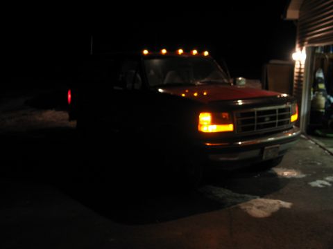 1995 Ford Bronco - A dark red Ford F-Series truck is parked in a driveway at night, with its headlights and cab lights illuminated.
