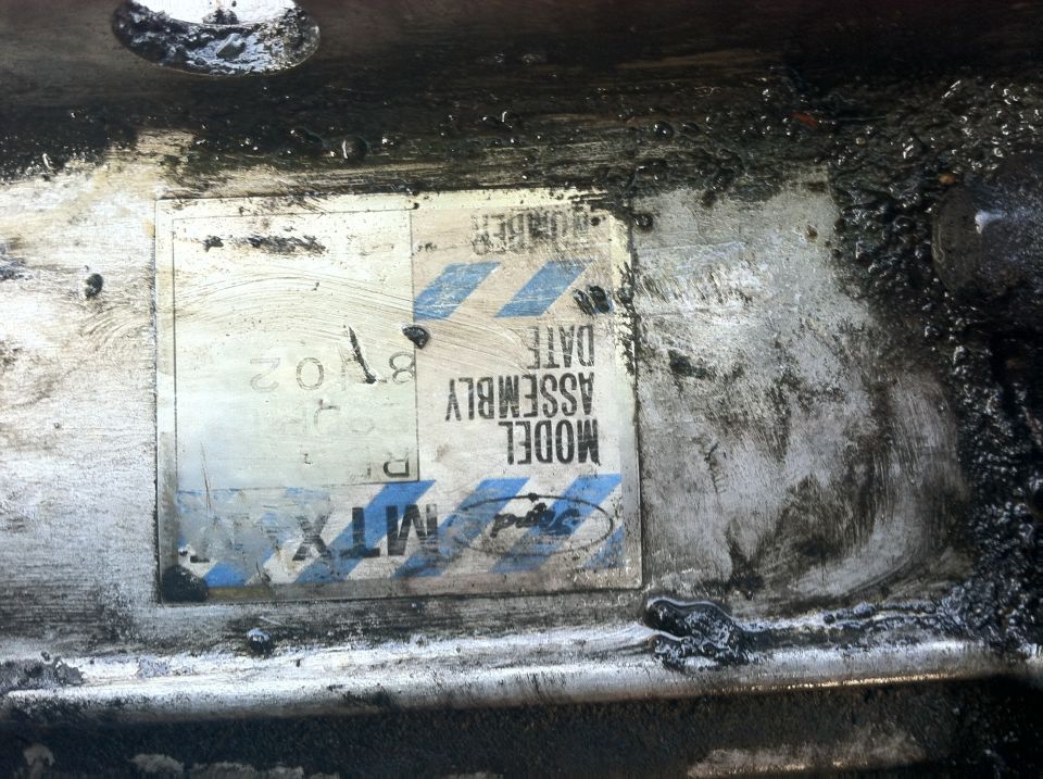 Ford MTX identification tag with model and assembly date fields on a greasy metal surface