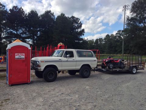 1979 Ford Bronco - Ford Bronco towing an ATV on a trailer, with a portable toilet nearby.