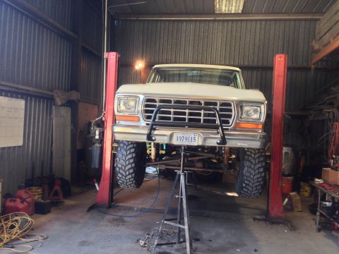 1979 Ford Bronco - A white 1979 Ford Bronco is raised on a hydraulic lift inside a workshop.