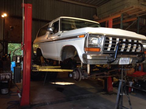1979 Ford Bronco - A white 1979 Ford Bronco is raised on a hydraulic lift in a workshop, revealing its undercarriage.