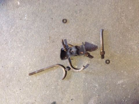 1979 Ford Bronco - Assorted metal parts, including a bracket and rods, lie on a concrete surface.