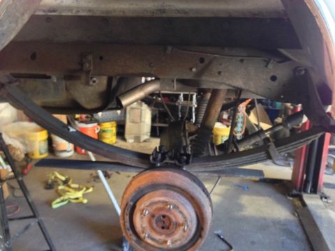 1979 Ford Bronco - The rear suspension and axle components of a vehicle are visible, with a rusty brake rotor and exhaust pipe.