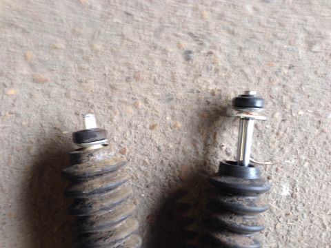1979 Ford Bronco - Close-up view of two automotive shock absorbers, one with a visible spring and metal rod, resting on a textured surface.