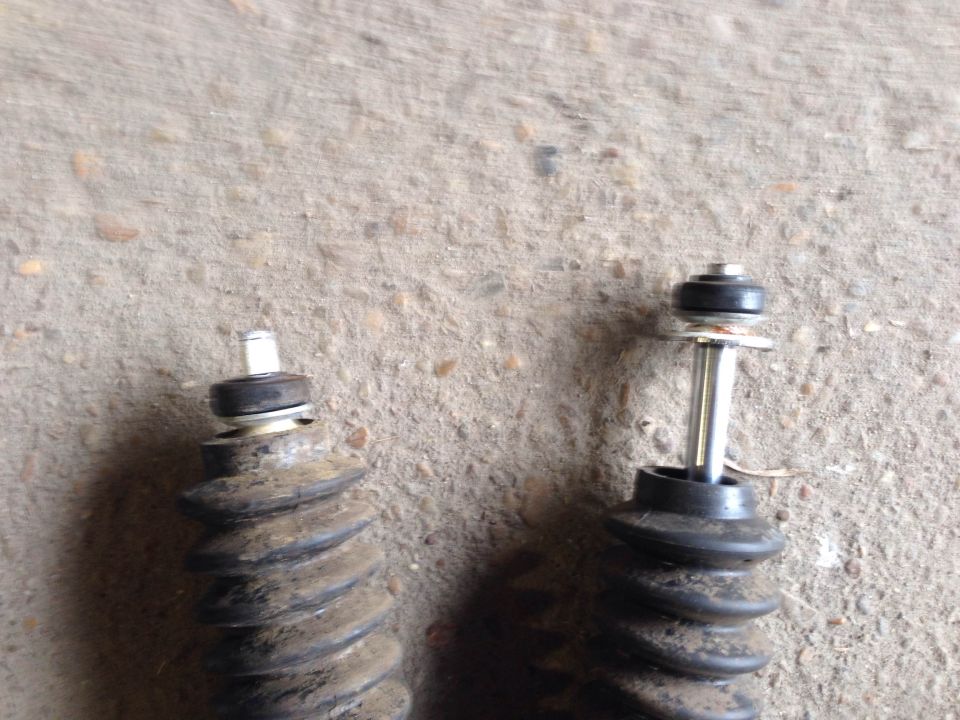 Two dirty shock absorbers with rubber bellows and metal shafts against a concrete surface