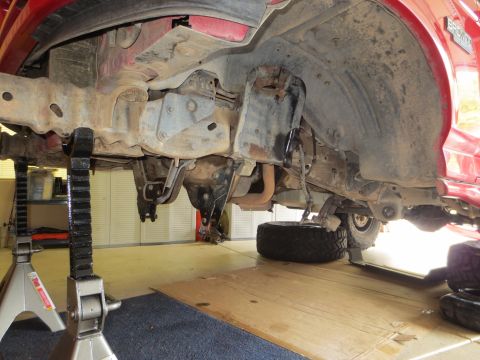 1996 Ford Bronco - Undercarriage of a red vehicle is elevated on jack stands for maintenance.
