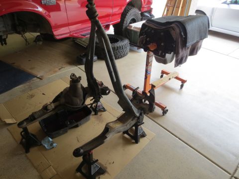 1996 Ford Bronco - A disassembled front axle assembly from a red Ford Bronco is supported by jack stands on a garage floor. An engine on an engine stand is vi…