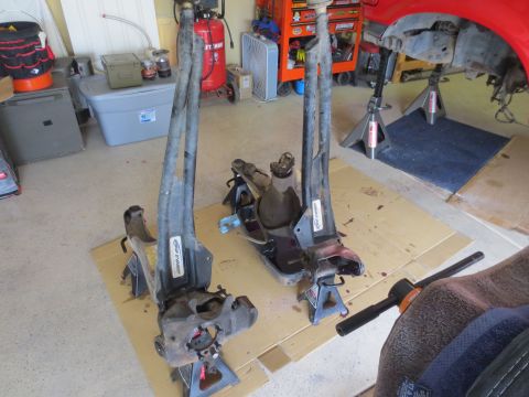1996 Ford Bronco - Two front suspension assemblies, likely from a 1996 Ford Bronco, are shown disassembled and resting on jack stands in a garage setting. One…