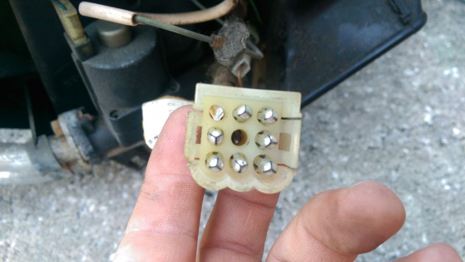 Close-up of a 9-pin electrical connector with silver pins, held by a hand.